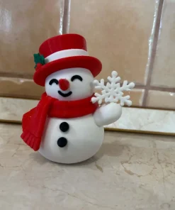 Người tuyết cầm bông tuyết in 3D đội mũ đỏ và quàng khăn đỏ